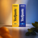 Two boxes of Teefpaste toothpaste, one yellow and one blue, on a blurred background.